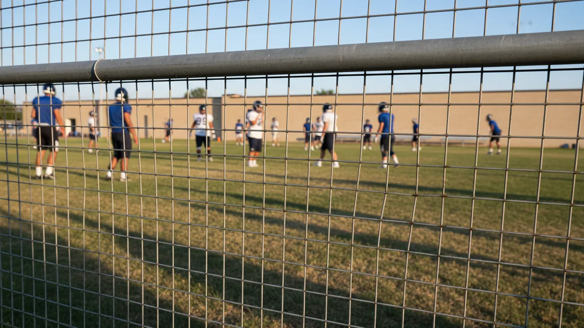 Equipo de fútbol americano practicando en un campo lateral, visto a través de una valla.