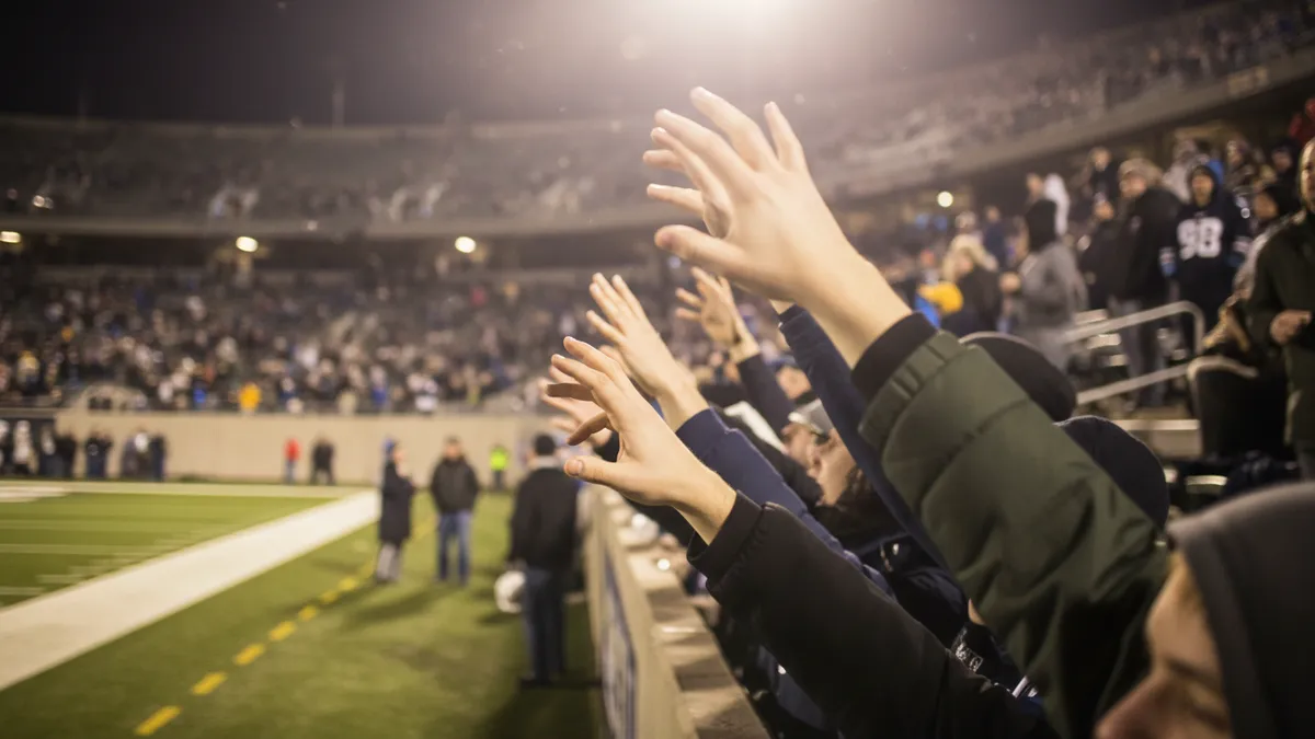 Manos levantadas de aficionados en un partido de la NFL por la noche.